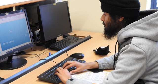 Man in a black turban and grey hoodie is busy working on a computer in an IT lab.