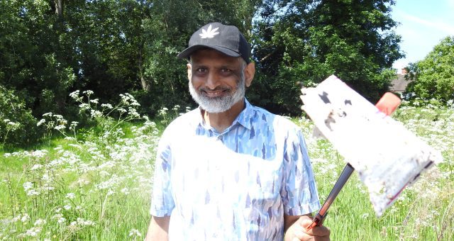 Learner is standing in front of a green field on a sunny day holding a litter-picker he has been using to pick up litter around his local area.
