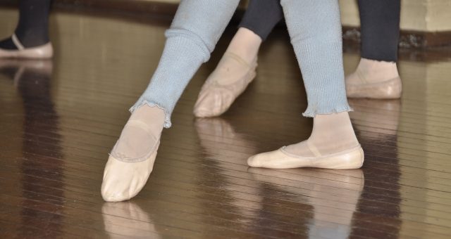 Image of a ballerina's feet in shoes, as they practice on a hard wooden floor.