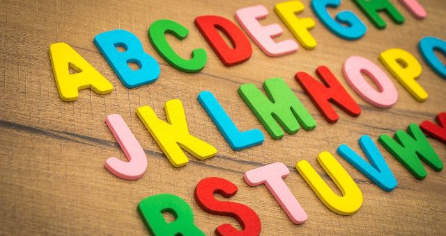 Image is a close-up of plastic alphabet letters laid out on a wooden table.