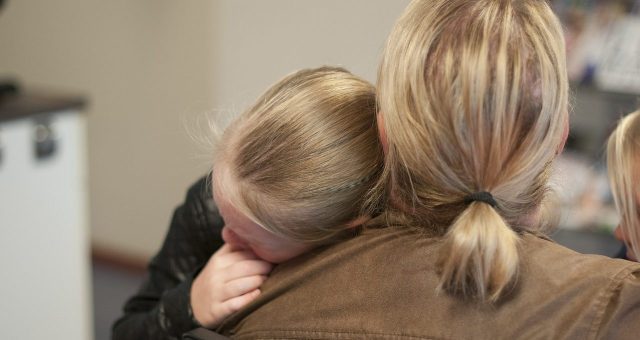 Image shows a parent comforting their child who is sleeping on their shoulder.