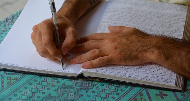 Image is a stock image showing a mans hands writing in a journal.