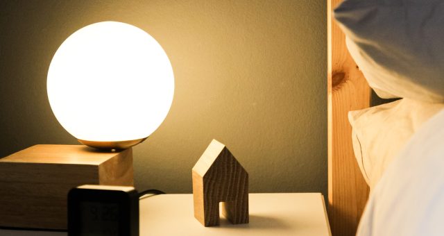 A bedside light creating a shadow of small wooden house and alarm clock.