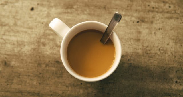 Image shows a mug of tea, taken from above as it rests on a wooden table.
