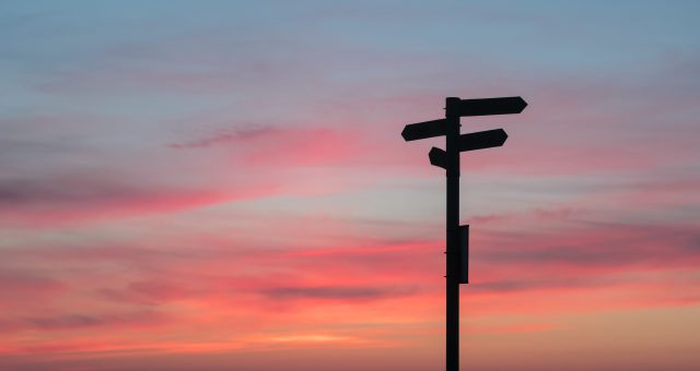 A photo of a directions sign post with sunset backdrop.
