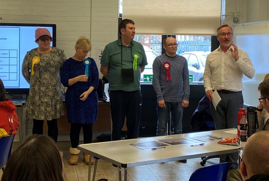 A group of learners stand at the front of the classroom in a line. They are each standing for election as part of a mock election for the empower course at Moira Adult Learning Centre in Loughborough.