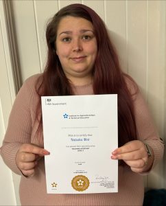 Photo shows Natasha, a graduate apprentice holding up the certificate for her teaching assistant apprenticeship. 