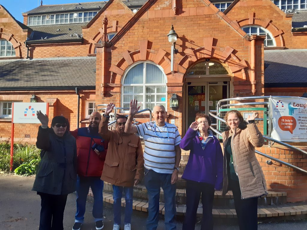 Image shows a group of learners standing in front of Charnwood Museum on a sunny day. The learners are smiling and waving at the camera. 