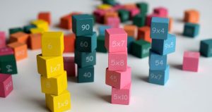 An image of colourful numbered cubes stacked and scattered on a table, showing multiplication and number facts as part of a hands-on maths activity.