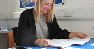 An image of a person seated at a desk, writing on paperwork in a classroom setting.