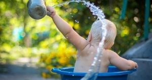 An image of a baby in a paddling pool throwing water