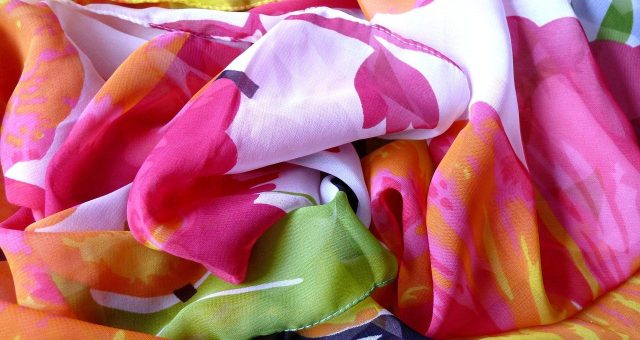 An image of a close-up of brightly coloured silk fabric featuring pink, orange, green and white floral patterns draped in soft folds.