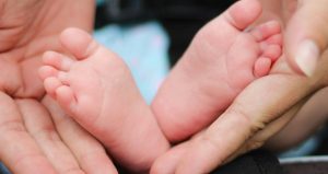 An image of a newborn baby’s feet resting gently in two adult hands.