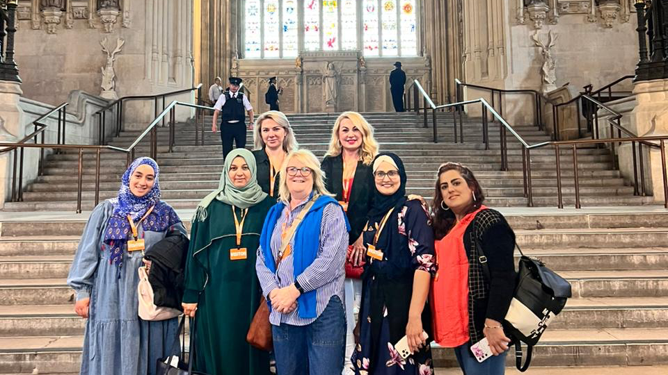 Photo of learners and tutor smiling in front of a grand stained-glass window at Westminster Hall in London.