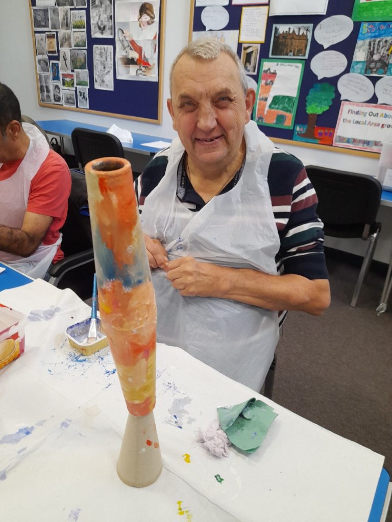 Image shows a learner smiling at the camera as he paints.