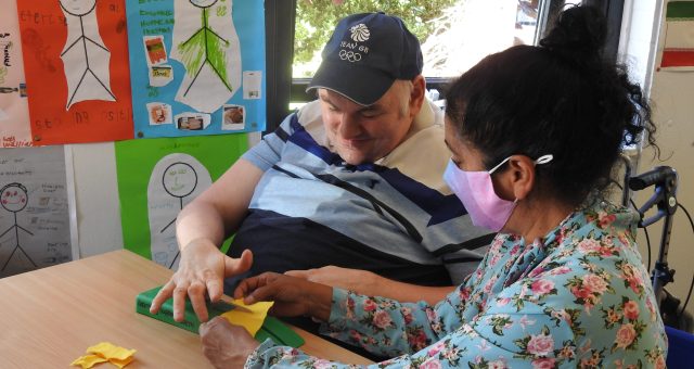 A learner is supported by a one to one support assistant to use adapted scissors to cut shapes from paper