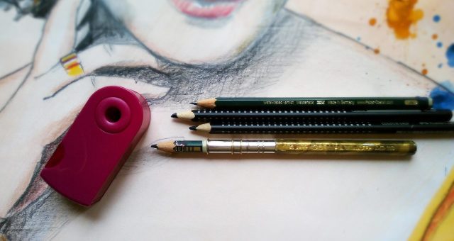 An image of drawing and painting tools, including pencils and a sharpener, placed on top of a partially completed mixed-media portrait artwork.