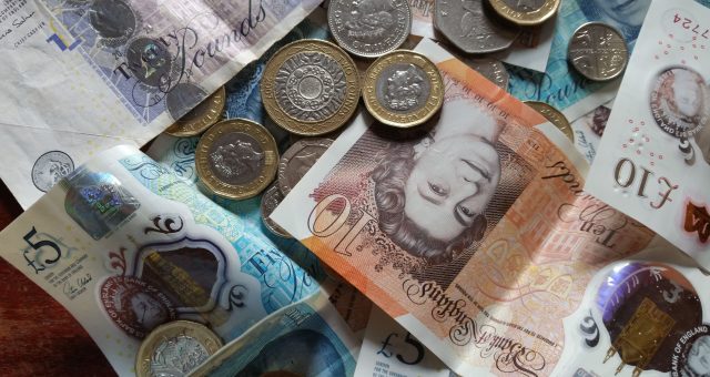 British pound banknotes and coins scattered across a surface, including £5, £10 and £20 notes mixed with various UK coins
